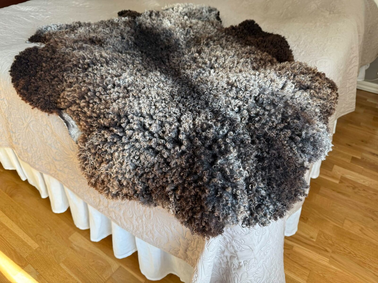 Lammskinn i naturvit ull draperat över en träbänk